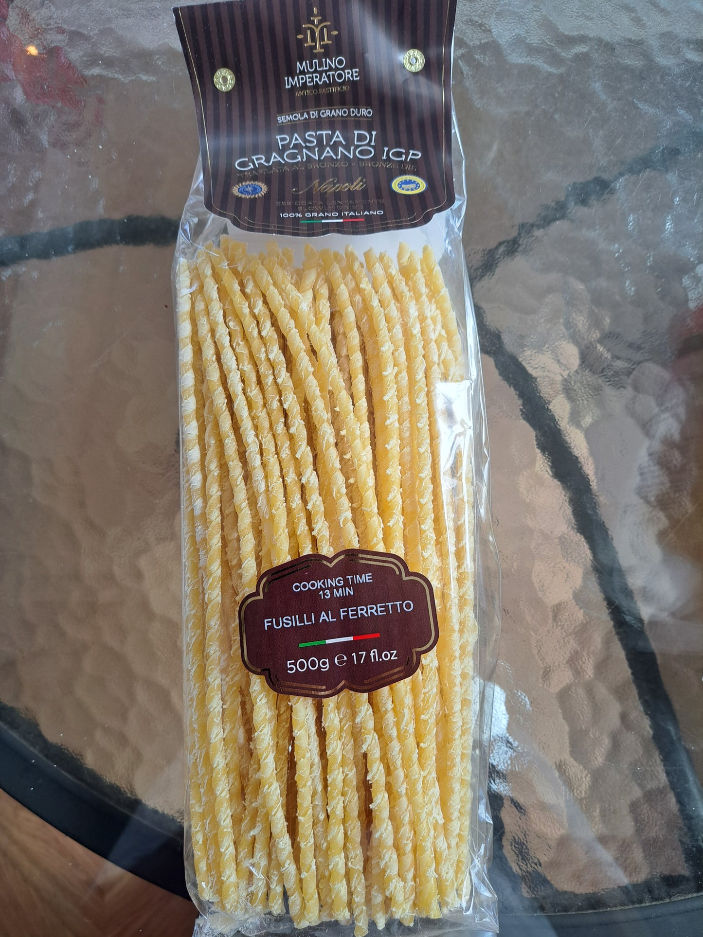 Packaged fusilli pasta with Mulino Imperatore branding on a glass surface.