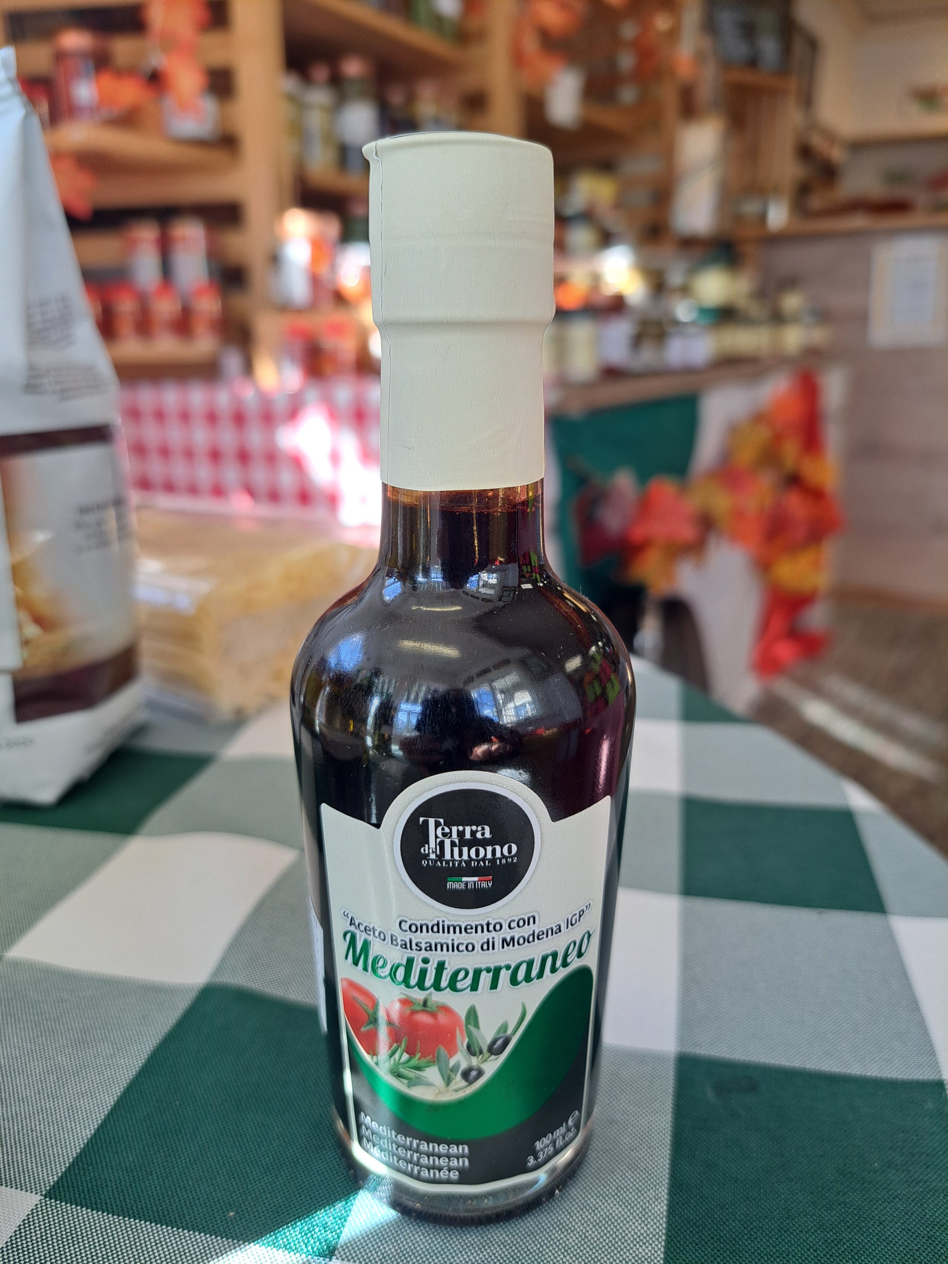 Bottle of Terra Italiana olive oil on a checkered tablecloth with a blurred store background