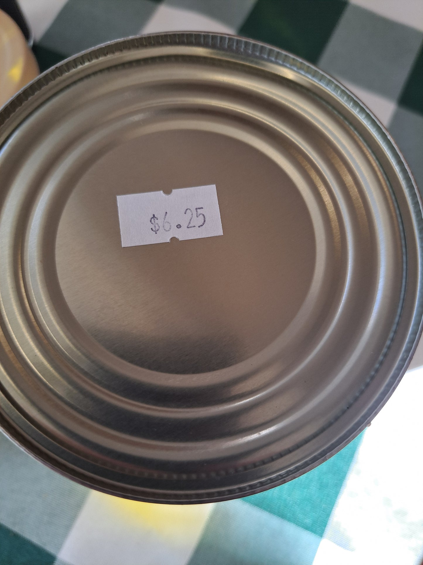 Close-up of a metal can lid with a small white label on a checkered surface.
